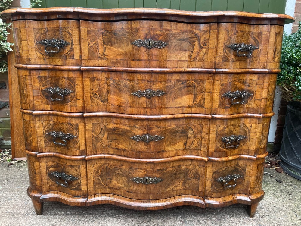 A mid-18th-century German Baroque walnut commode featuring a shaped serpentine front, four long drawers with figured wood veneers, and ornate cast brass handles. View IX