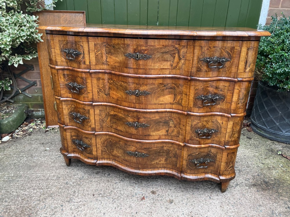 A mid-18th-century German Baroque walnut commode featuring a shaped serpentine front, four long drawers with figured wood veneers, and ornate cast brass handles. View XV