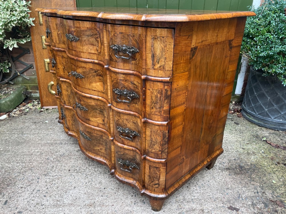 A mid-18th-century German Baroque walnut commode featuring a shaped serpentine front, four long drawers with figured wood veneers, and ornate cast brass handles. View XVII