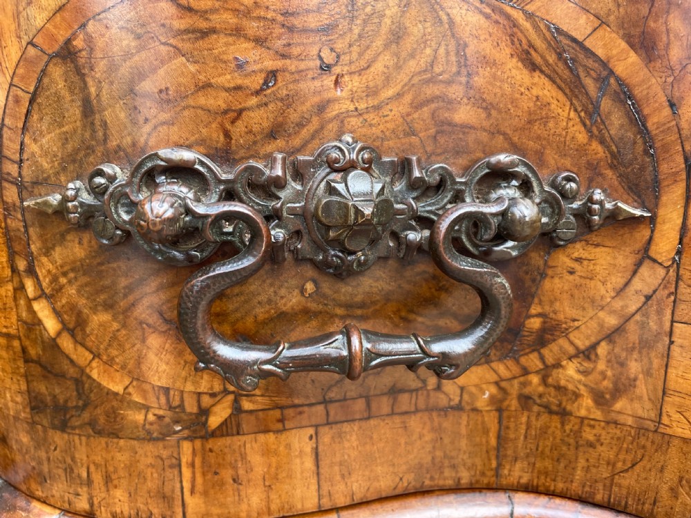 A mid-18th-century German Baroque walnut commode featuring a shaped serpentine front, four long drawers with figured wood veneers, and ornate cast brass handles. View XIX