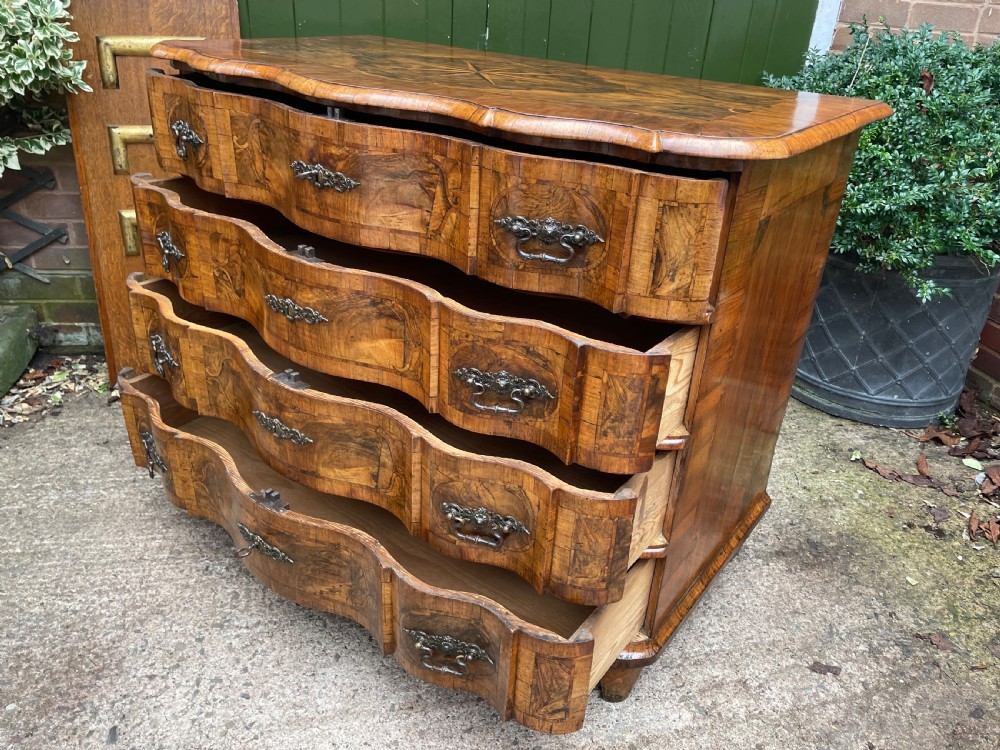 A mid-18th-century German Baroque walnut commode featuring a shaped serpentine front, four long drawers with figured wood veneers, and ornate cast brass handles. View XX