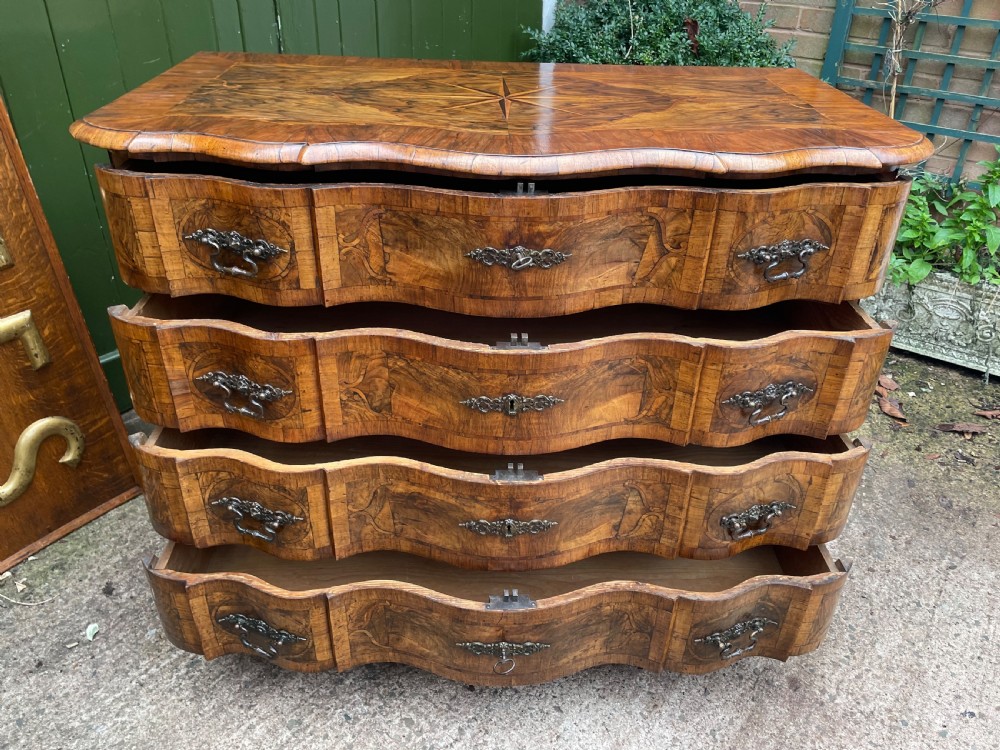 A mid-18th-century German Baroque walnut commode featuring a shaped serpentine front, four long drawers with figured wood veneers, and ornate cast brass handles. View XXI