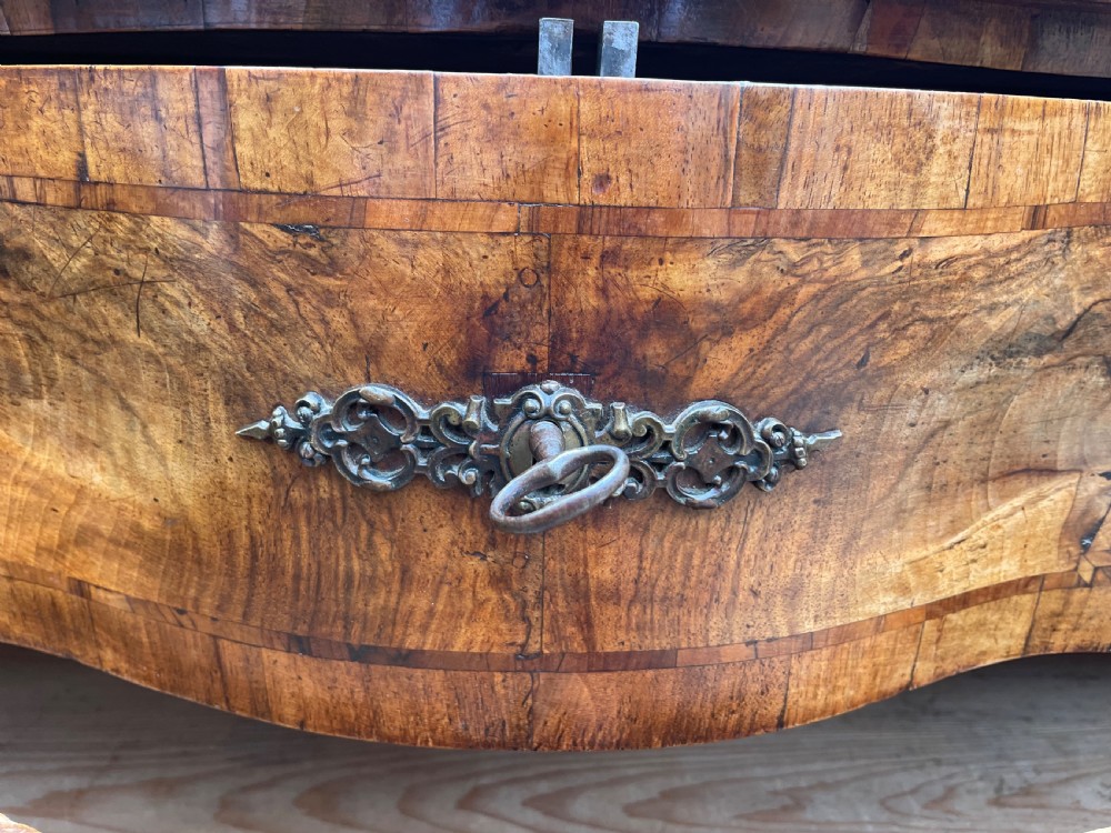 A mid-18th-century German Baroque walnut commode featuring a shaped serpentine front, four long drawers with figured wood veneers, and ornate cast brass handles. View XXII