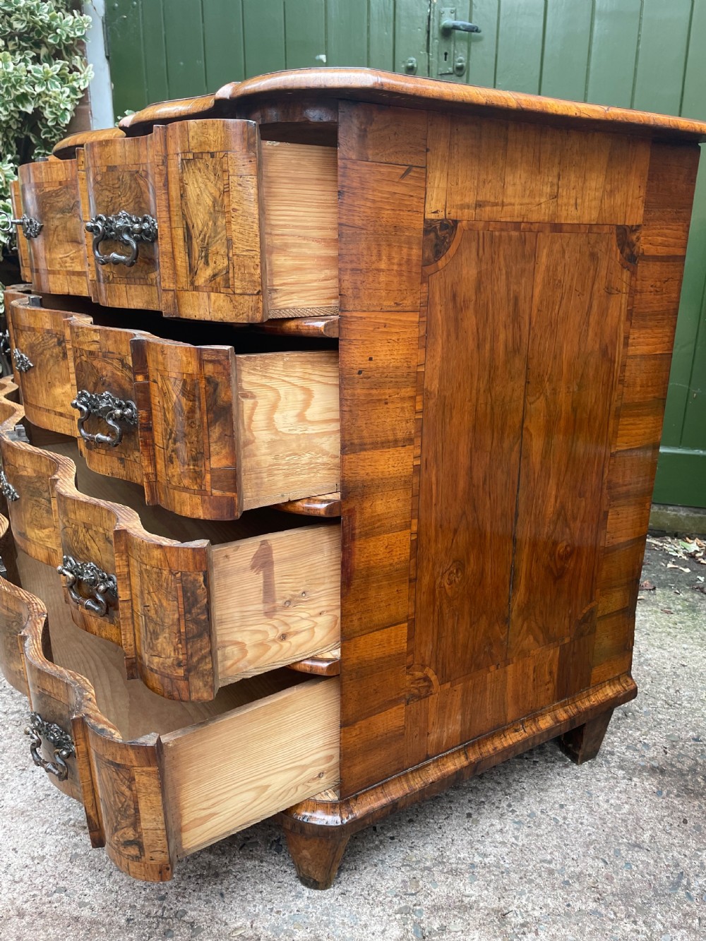 A mid-18th-century German Baroque walnut commode featuring a shaped serpentine front, four long drawers with figured wood veneers, and ornate cast brass handles. View XXIV
