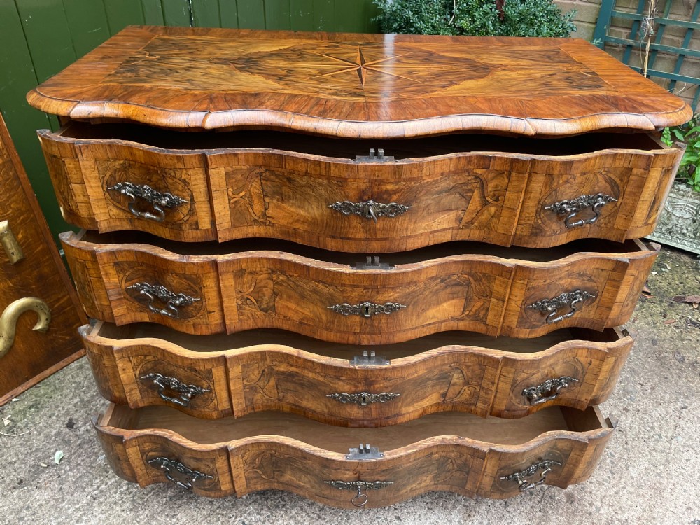A mid-18th-century German Baroque walnut commode featuring a shaped serpentine front, four long drawers with figured wood veneers, and ornate cast brass handles. View XXV