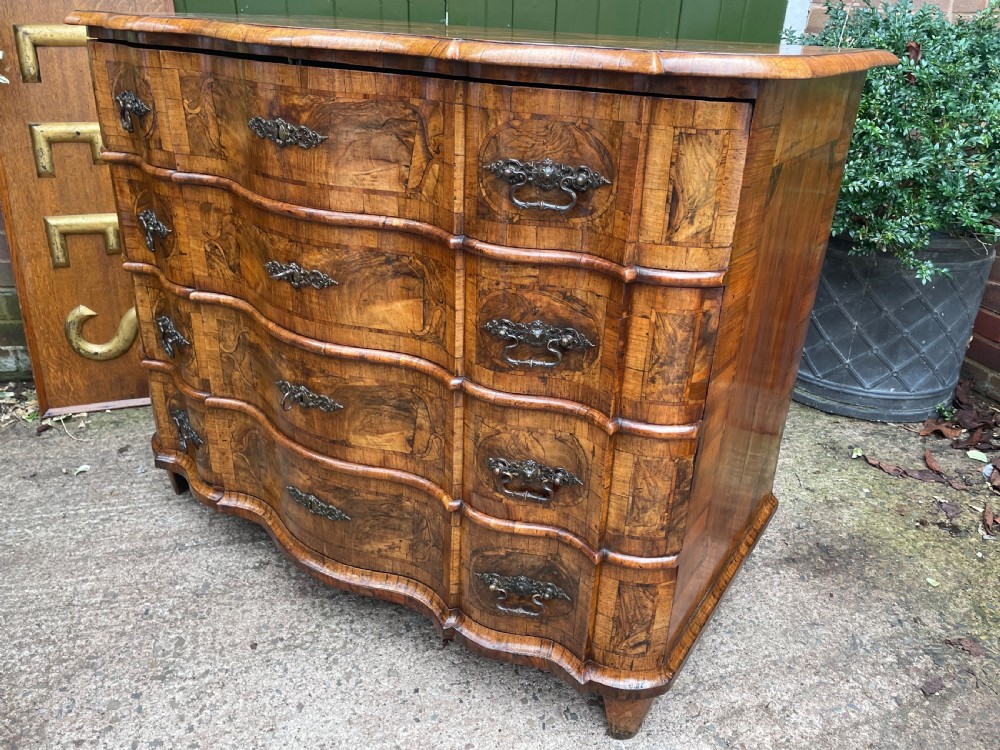 A mid-18th-century German Baroque walnut commode featuring a shaped serpentine front, four long drawers with figured wood veneers, and ornate cast brass handles. View XXVI