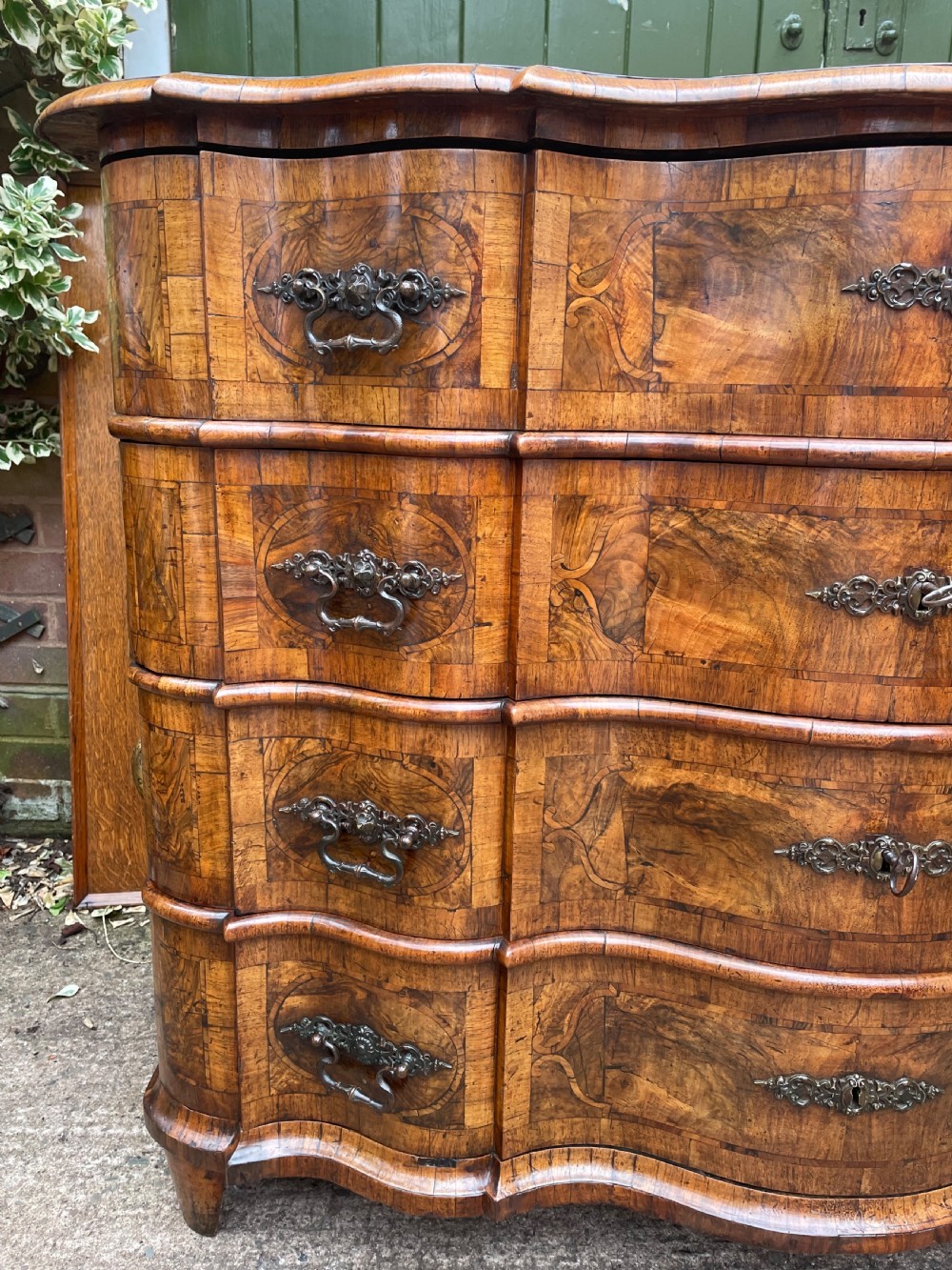 A mid-18th-century German Baroque walnut commode featuring a shaped serpentine front, four long drawers with figured wood veneers, and ornate cast brass handles. View XXX