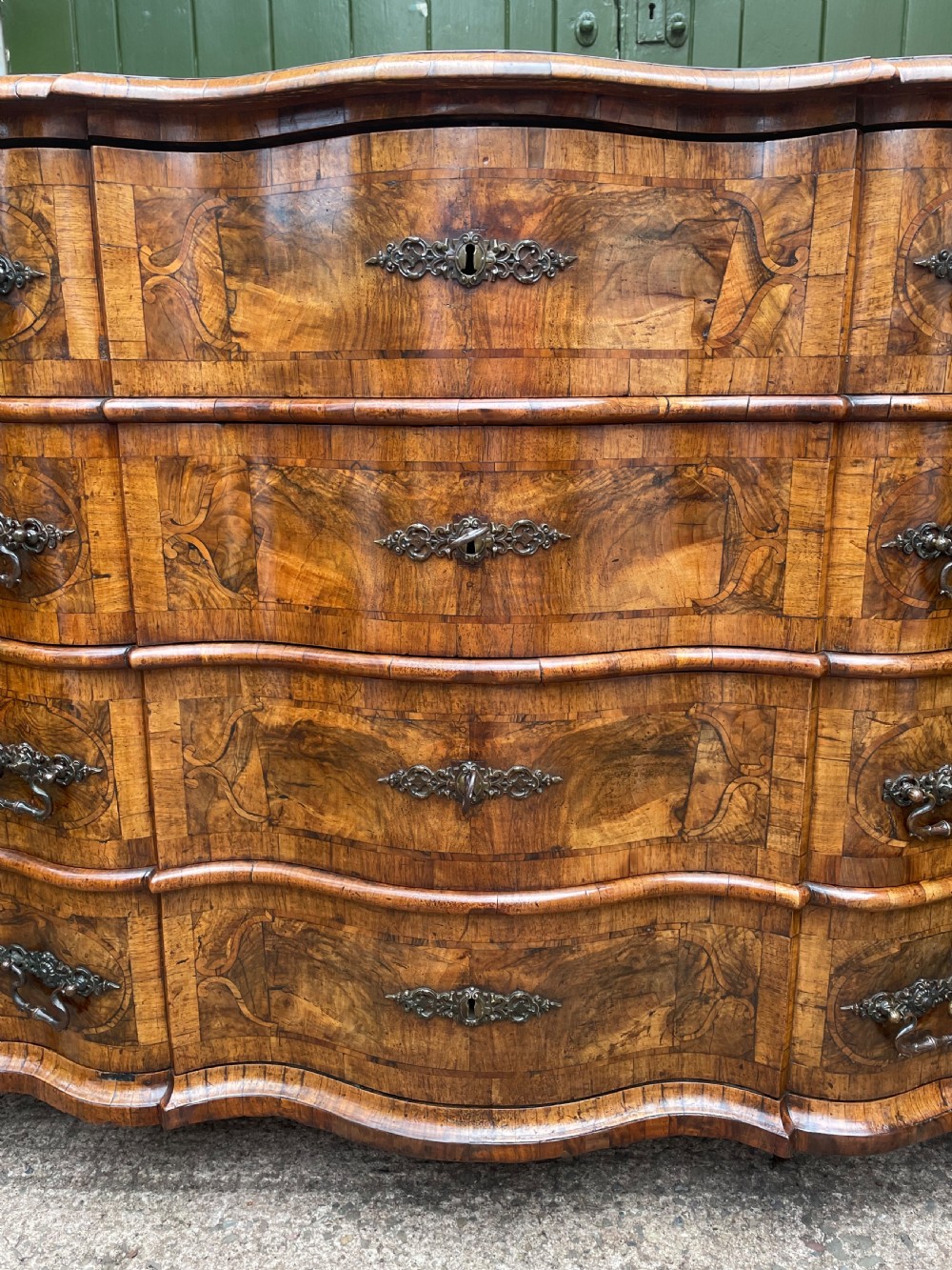 A mid-18th-century German Baroque walnut commode featuring a shaped serpentine front, four long drawers with figured wood veneers, and ornate cast brass handles. View XXXI