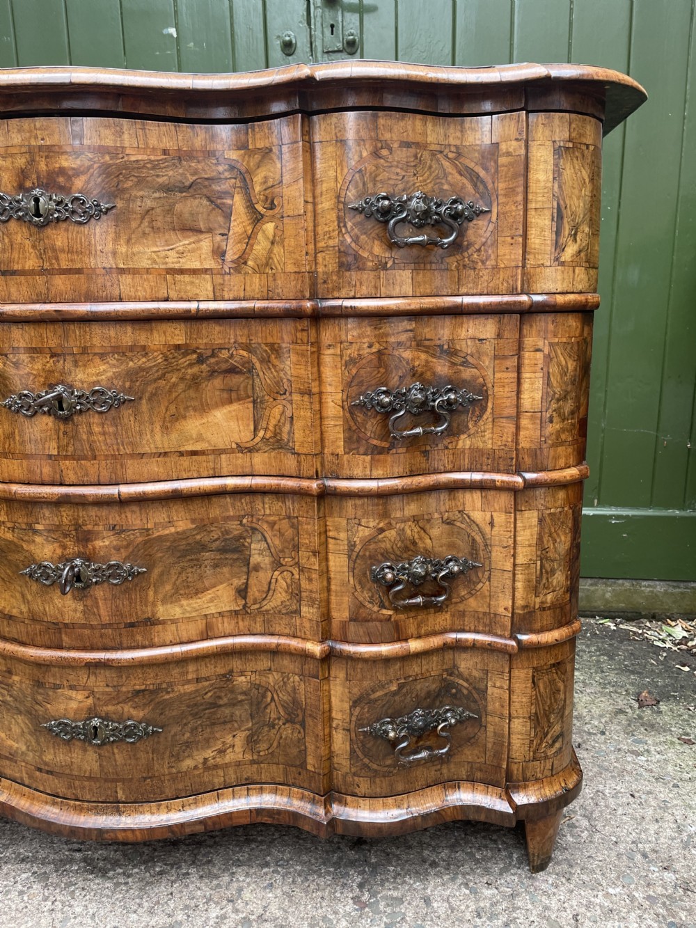 A mid-18th-century German Baroque walnut commode featuring a shaped serpentine front, four long drawers with figured wood veneers, and ornate cast brass handles. View XXXII