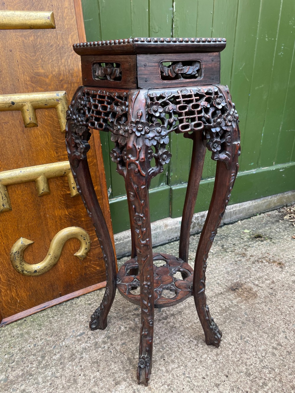 A late nineteenth-century Chinese carved dark hardwood plant stand featuring intricate floral openwork aprons, slender curved legs, and a lower circular tier.