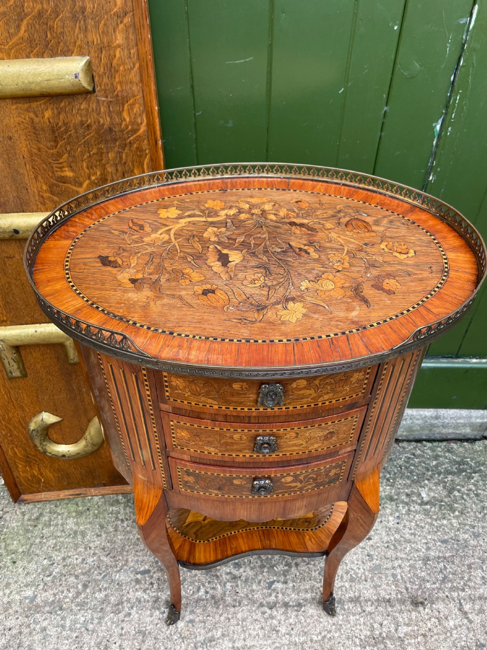 A late nineteenth-century French oval marquetry table featuring three drawers with floral inlay, a pierced brass gallery top, and a lower shelf decorated with a marquetry book design. View II