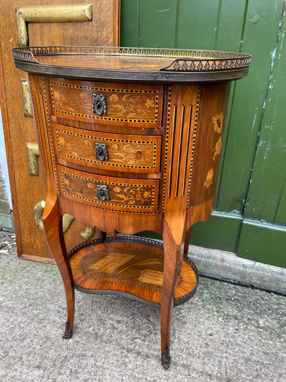 A late nineteenth-century French oval marquetry table featuring three drawers with floral inlay, a pierced brass gallery top, and a lower shelf decorated with a marquetry book design. View III