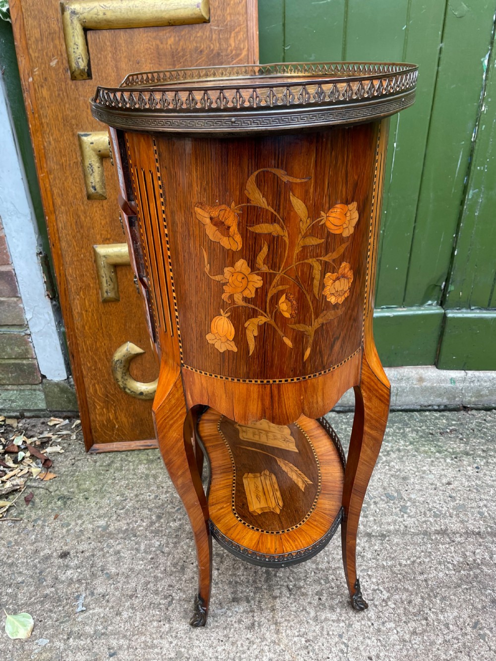 A late nineteenth-century French oval marquetry table featuring three drawers with floral inlay, a pierced brass gallery top, and a lower shelf decorated with a marquetry book design. View V