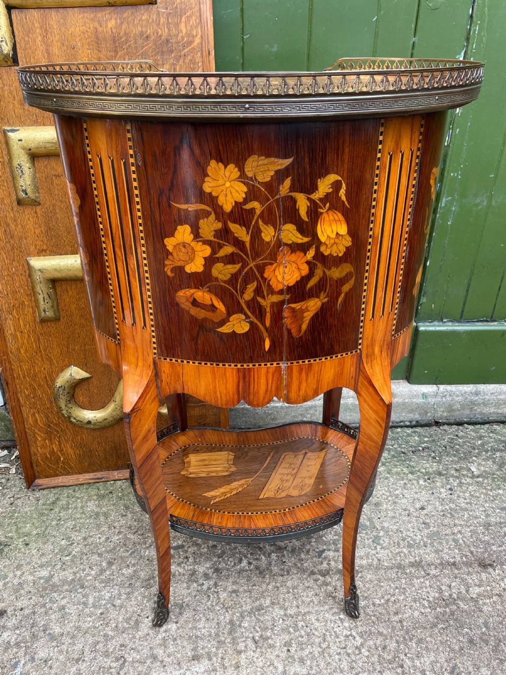 A late nineteenth-century French oval marquetry table featuring three drawers with floral inlay, a pierced brass gallery top, and a lower shelf decorated with a marquetry book design. View VI