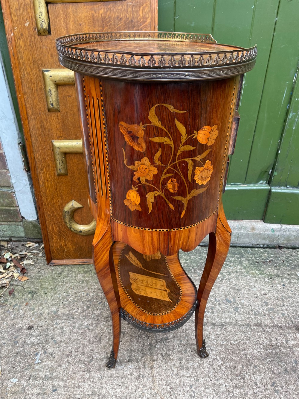 A late nineteenth-century French oval marquetry table featuring three drawers with floral inlay, a pierced brass gallery top, and a lower shelf decorated with a marquetry book design. View VII