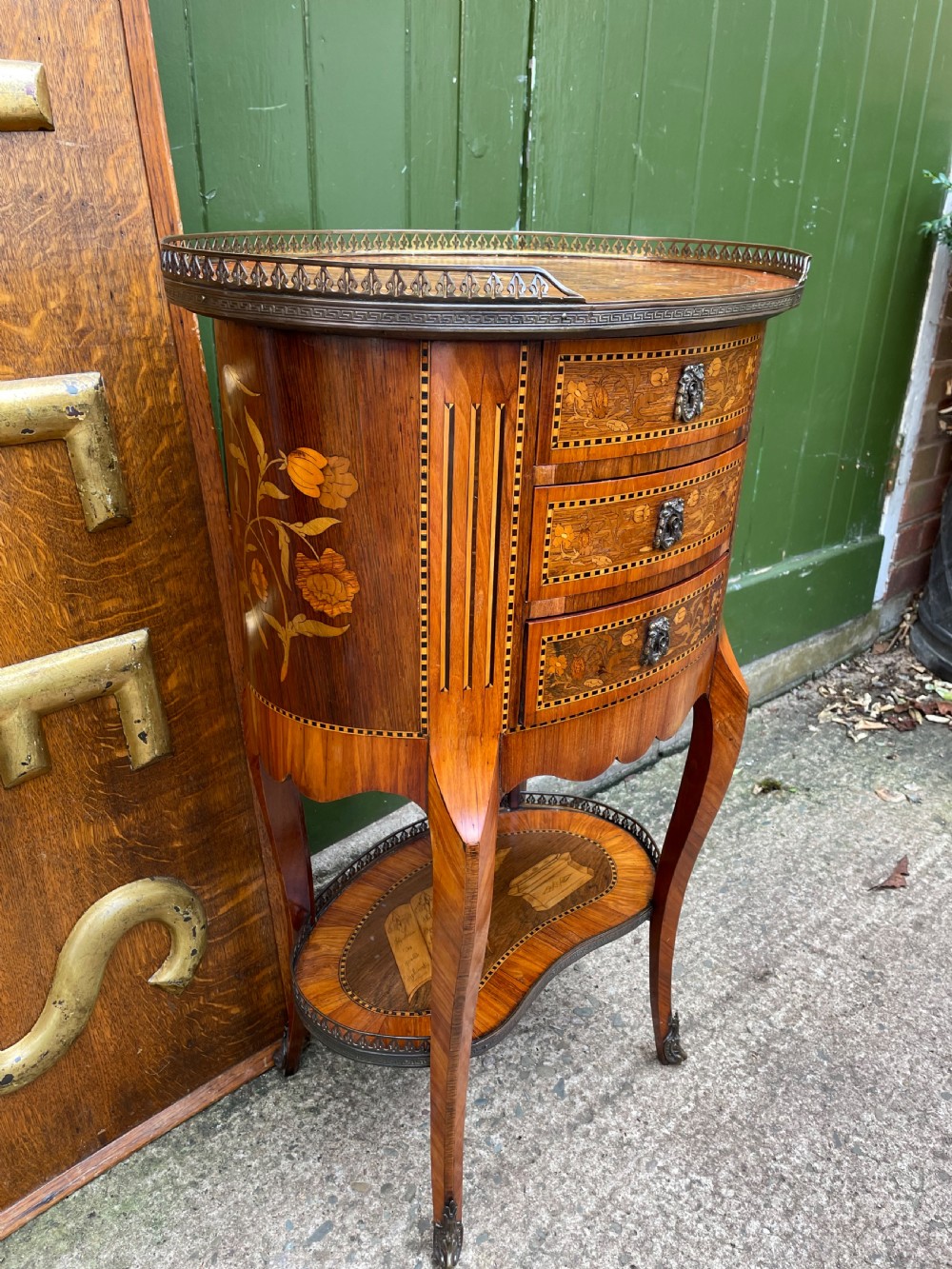 A late nineteenth-century French oval marquetry table featuring three drawers with floral inlay, a pierced brass gallery top, and a lower shelf decorated with a marquetry book design. View VIII