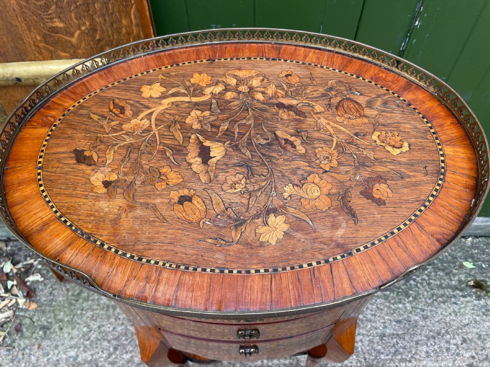 A late nineteenth-century French oval marquetry table featuring three drawers with floral inlay, a pierced brass gallery top, and a lower shelf decorated with a marquetry book design. View XI