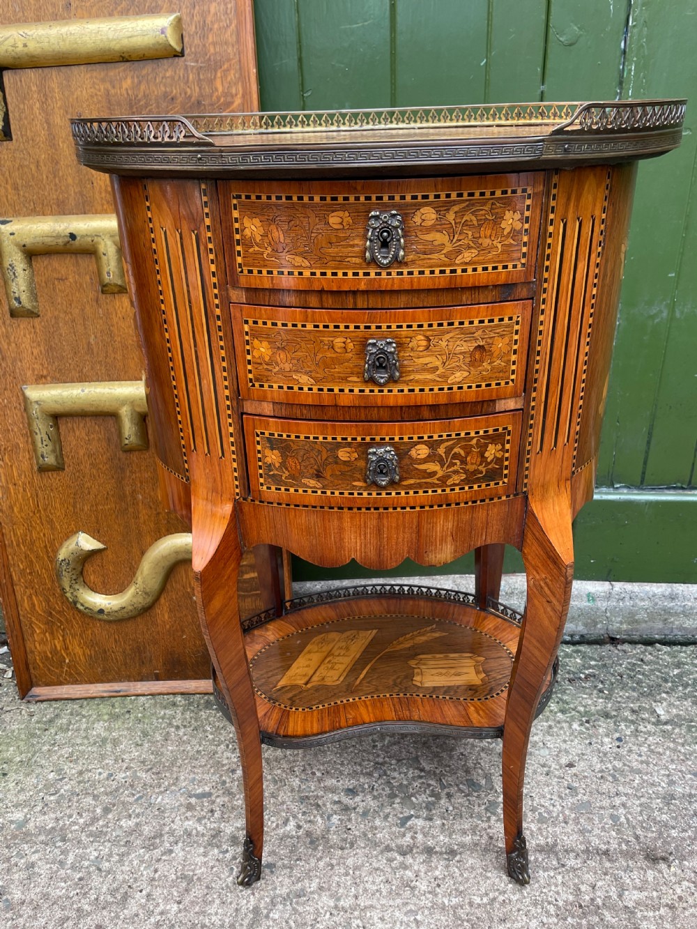 A late nineteenth-century French oval marquetry table featuring three drawers with floral inlay, a pierced brass gallery top, and a lower shelf decorated with a marquetry book design. View XII