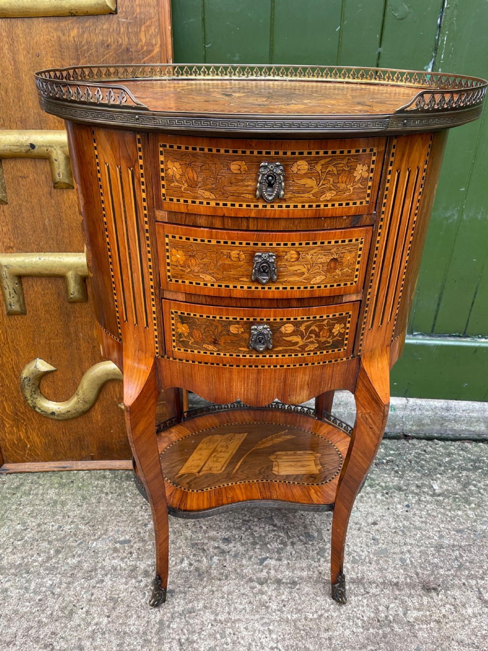 A late nineteenth-century French oval marquetry table featuring three drawers with floral inlay, a pierced brass gallery top, and a lower shelf decorated with a marquetry book design. View XIV