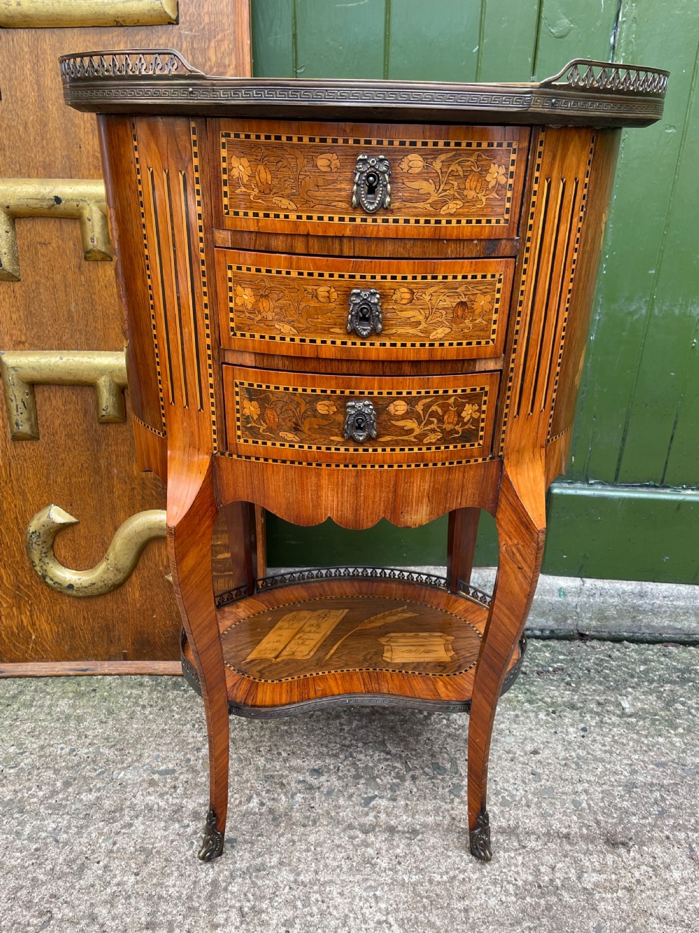A late nineteenth-century French oval marquetry table featuring three drawers with floral inlay, a pierced brass gallery top, and a lower shelf decorated with a marquetry book design. View XVI