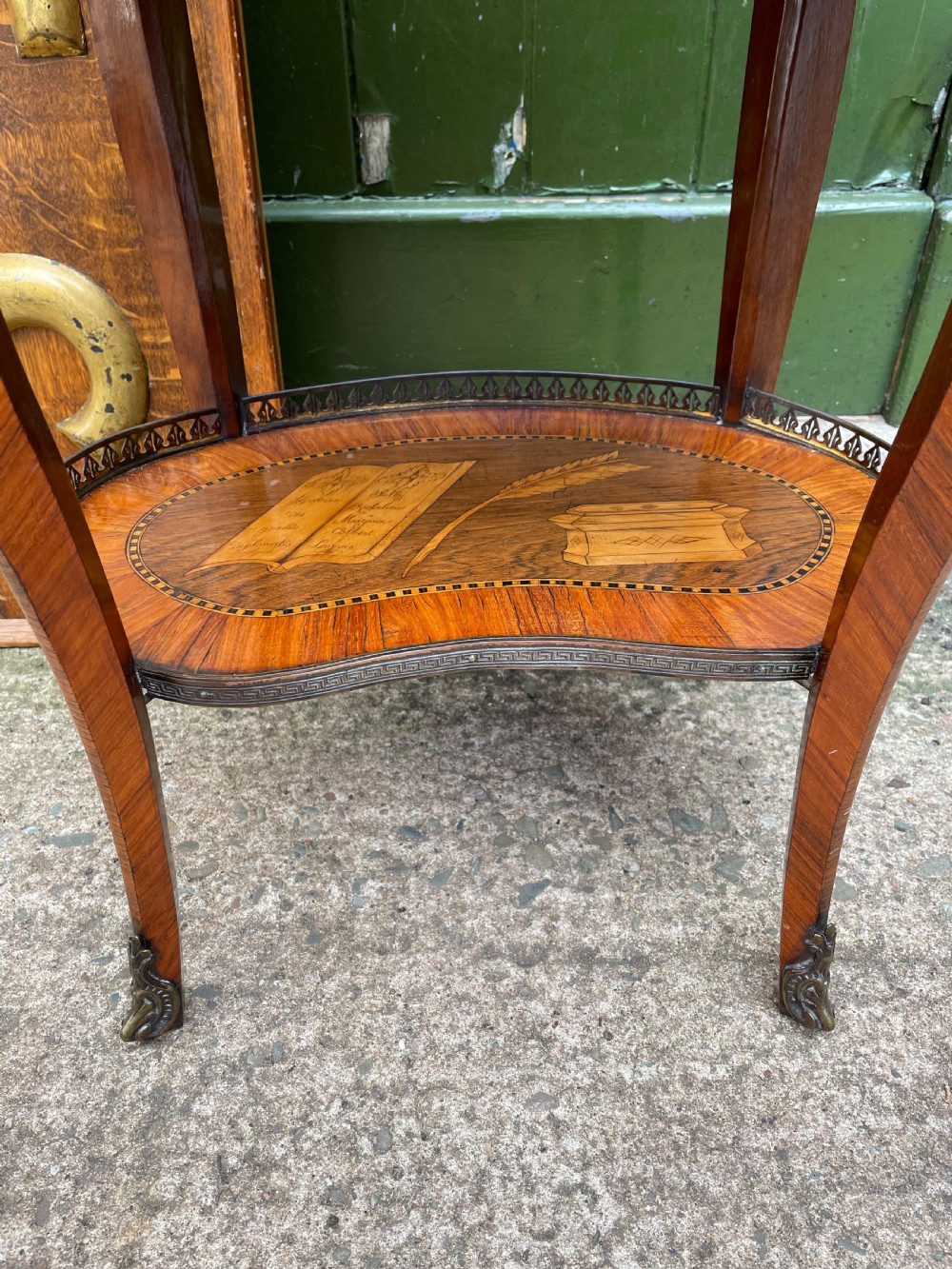 A late nineteenth-century French oval marquetry table featuring three drawers with floral inlay, a pierced brass gallery top, and a lower shelf decorated with a marquetry book design. View XVII