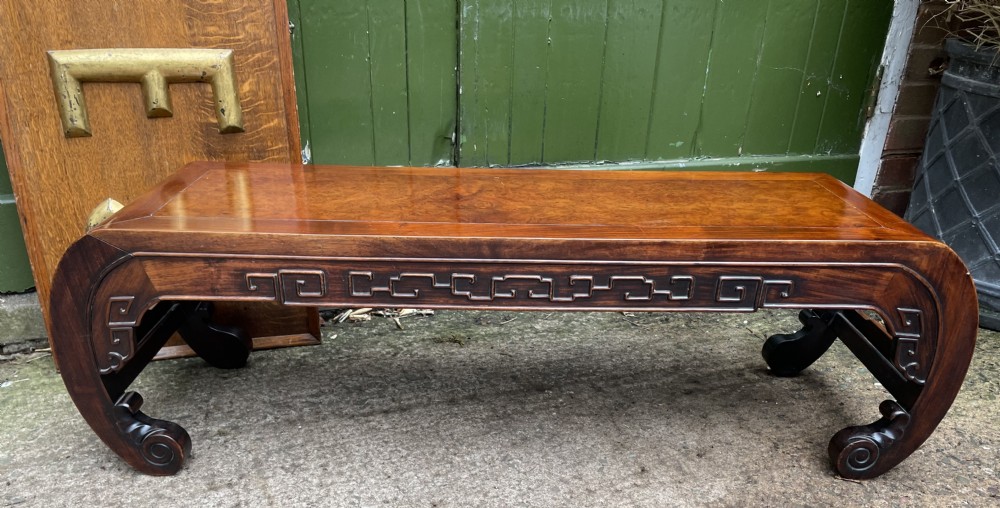 A low Chinese Qing Dynasty hardwood kang table featuring carved key-fret aprons and inward-curved scroll legs.