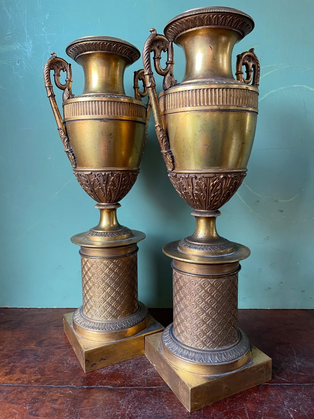 A pair of early 19th-century French gilt-bronze Neoclassical urns featuring scrolled handles, acanthus leaf relief, and diaper-patterned cylindrical plinths. View II