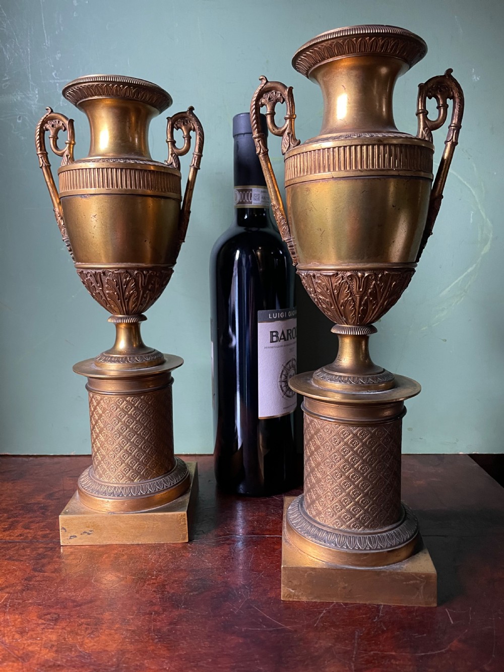 A pair of early 19th-century French gilt-bronze Neoclassical urns featuring scrolled handles, acanthus leaf relief, and diaper-patterned cylindrical plinths. View IV