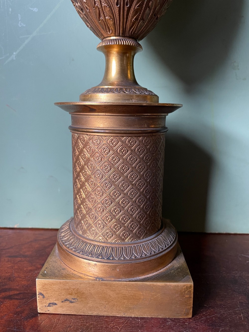 A pair of early 19th-century French gilt-bronze Neoclassical urns featuring scrolled handles, acanthus leaf relief, and diaper-patterned cylindrical plinths. View XI