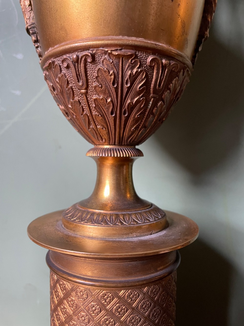 A pair of early 19th-century French gilt-bronze Neoclassical urns featuring scrolled handles, acanthus leaf relief, and diaper-patterned cylindrical plinths. View XII