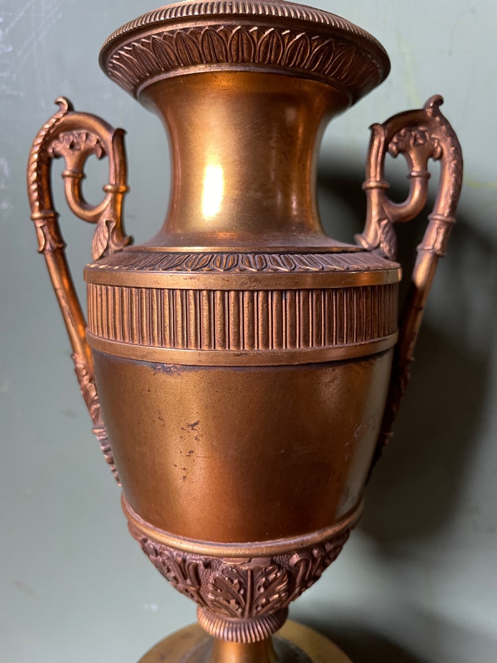 A pair of early 19th-century French gilt-bronze Neoclassical urns featuring scrolled handles, acanthus leaf relief, and diaper-patterned cylindrical plinths. View XIII