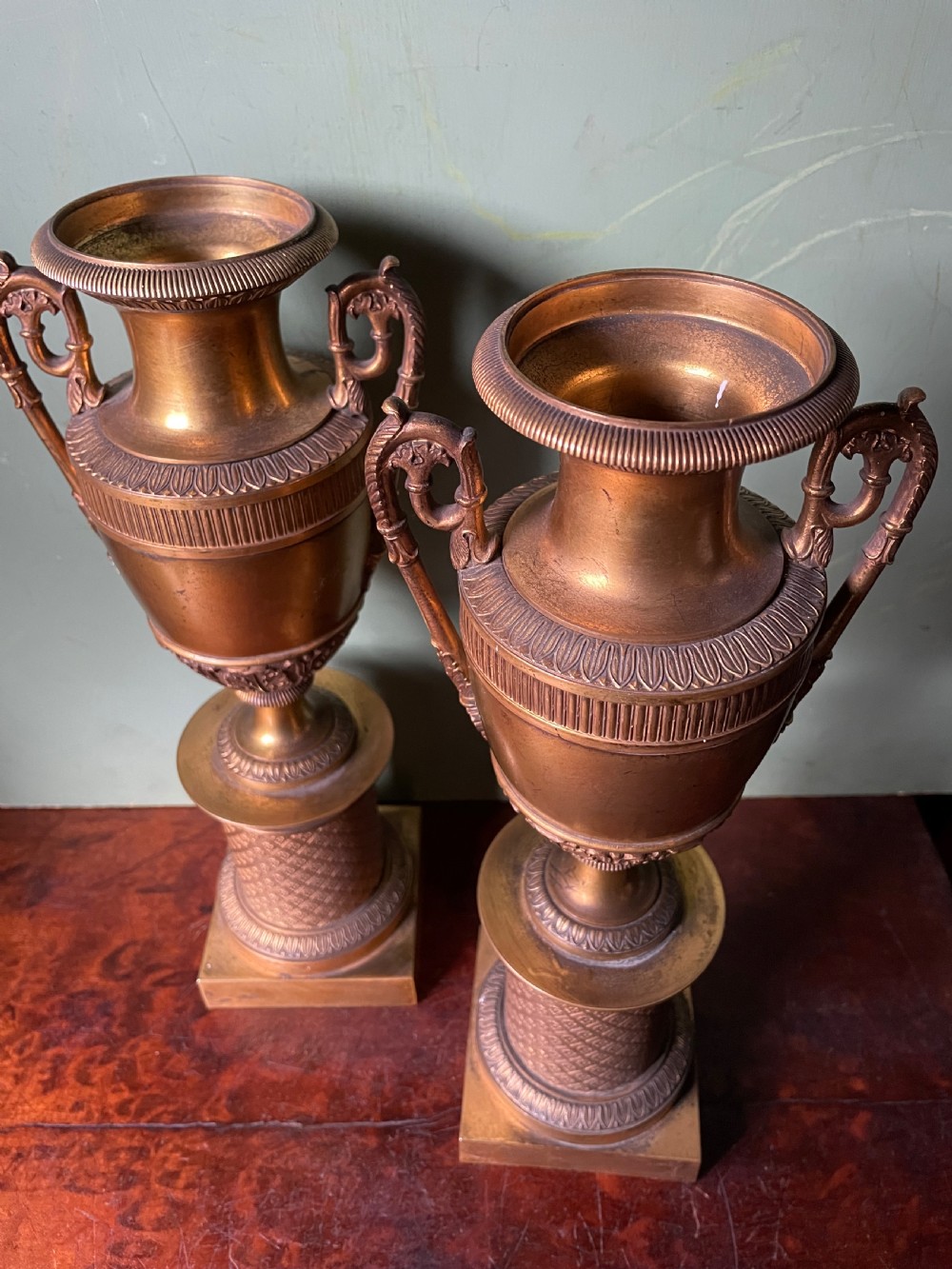 A pair of early 19th-century French gilt-bronze Neoclassical urns featuring scrolled handles, acanthus leaf relief, and diaper-patterned cylindrical plinths. View XV