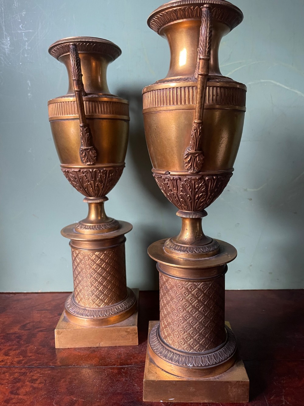 A pair of early 19th-century French gilt-bronze Neoclassical urns featuring scrolled handles, acanthus leaf relief, and diaper-patterned cylindrical plinths. View XVIII