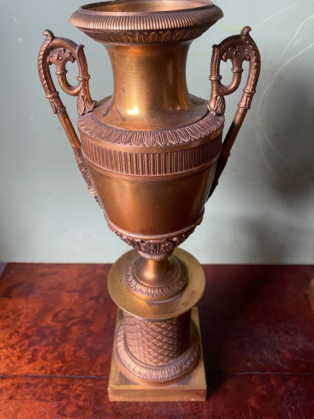 A pair of early 19th-century French gilt-bronze Neoclassical urns featuring scrolled handles, acanthus leaf relief, and diaper-patterned cylindrical plinths. View XIX
