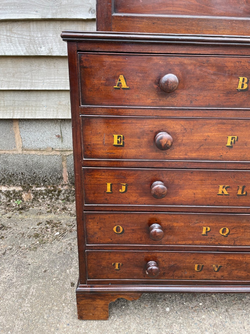 A late eighteenth-century George III mahogany estate cabinet featuring upper panel doors above drawers with gilded alphabetical lettering. View IV