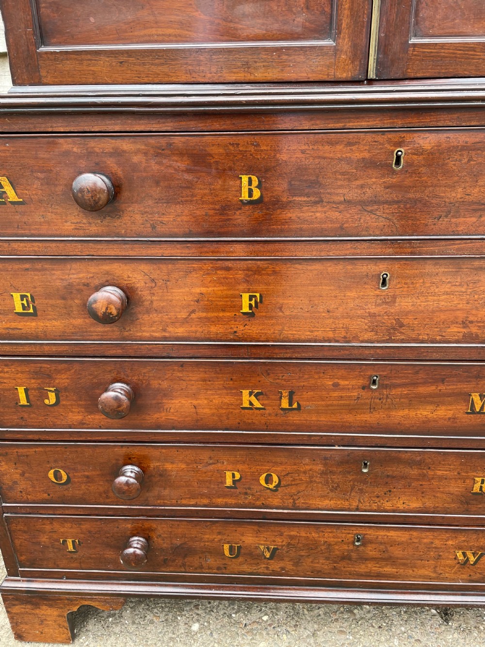 A late eighteenth-century George III mahogany estate cabinet featuring upper panel doors above drawers with gilded alphabetical lettering. View V