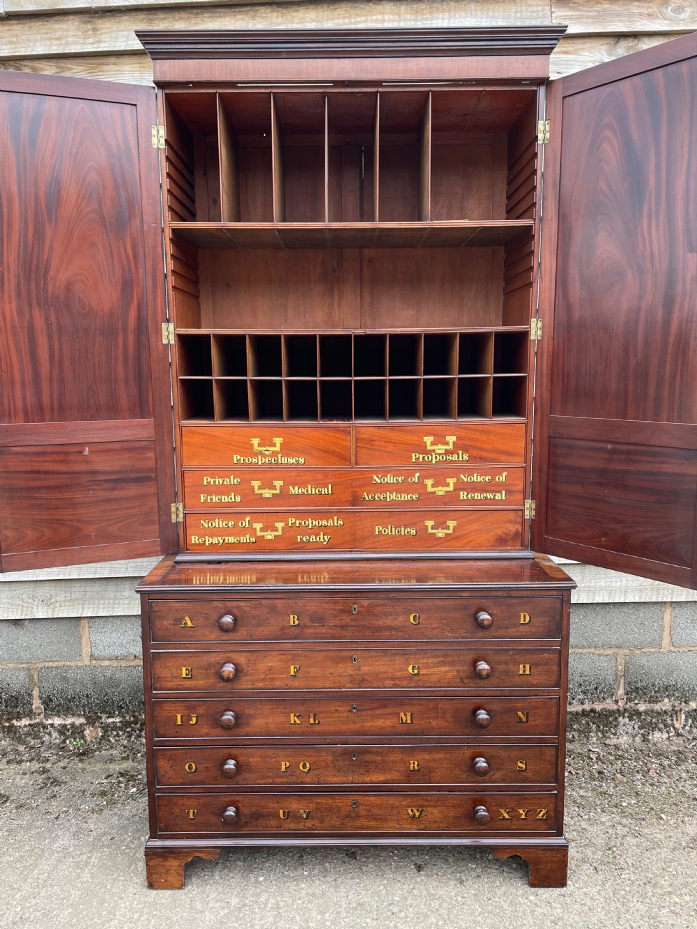 A late eighteenth-century George III mahogany estate cabinet featuring upper panel doors above drawers with gilded alphabetical lettering. View XIV