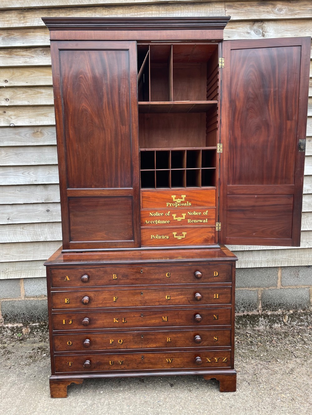 A late eighteenth-century George III mahogany estate cabinet featuring upper panel doors above drawers with gilded alphabetical lettering. View XV