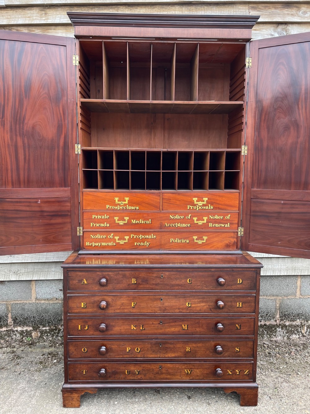 A late eighteenth-century George III mahogany estate cabinet featuring upper panel doors above drawers with gilded alphabetical lettering. View XX
