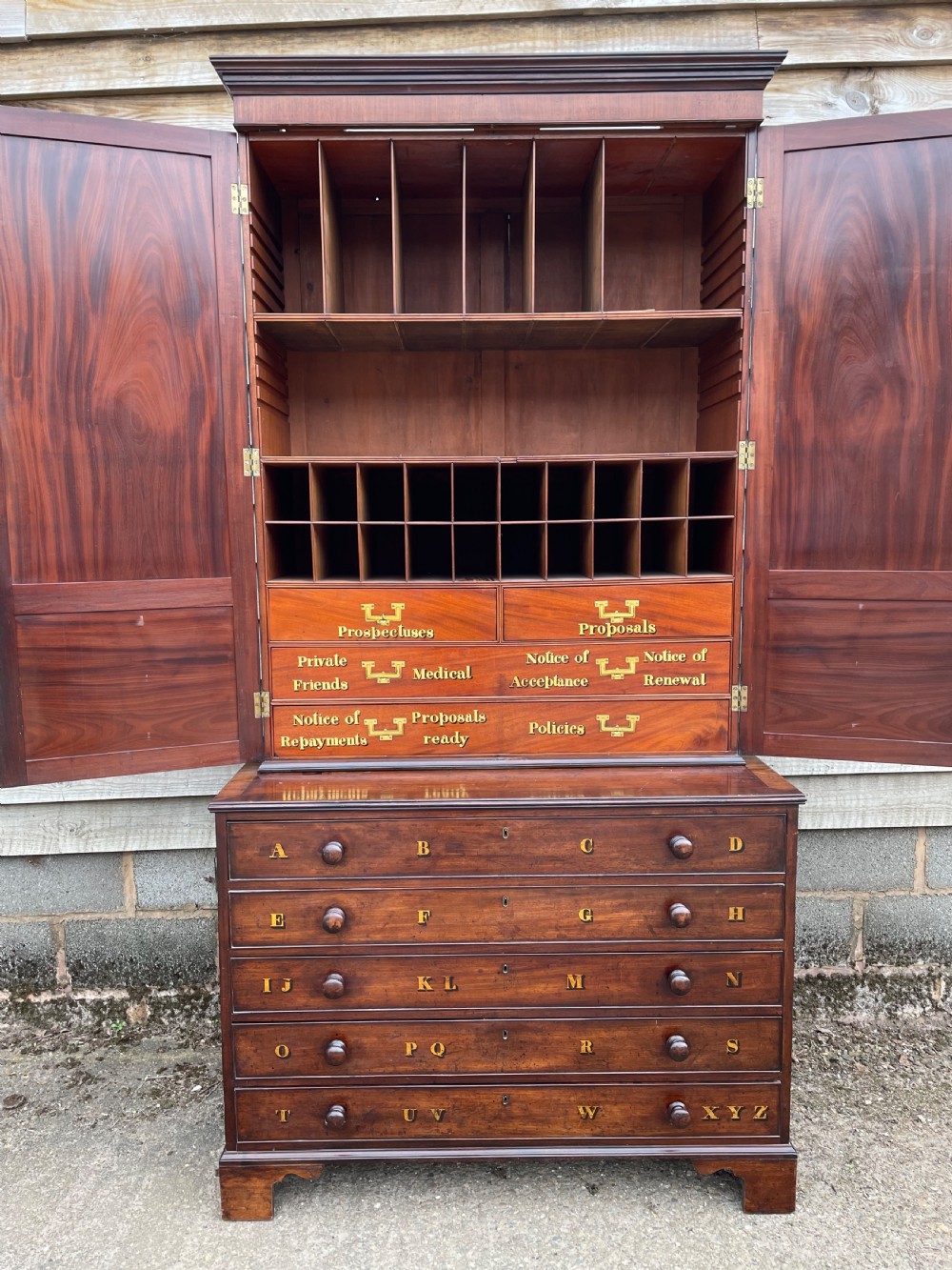 A late eighteenth-century George III mahogany estate cabinet featuring upper panel doors above drawers with gilded alphabetical lettering. View XXIV