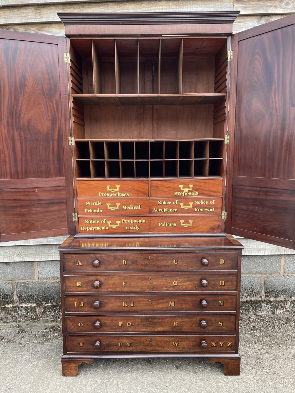 A late eighteenth-century George III mahogany estate cabinet featuring upper panel doors above drawers with gilded alphabetical lettering. View II