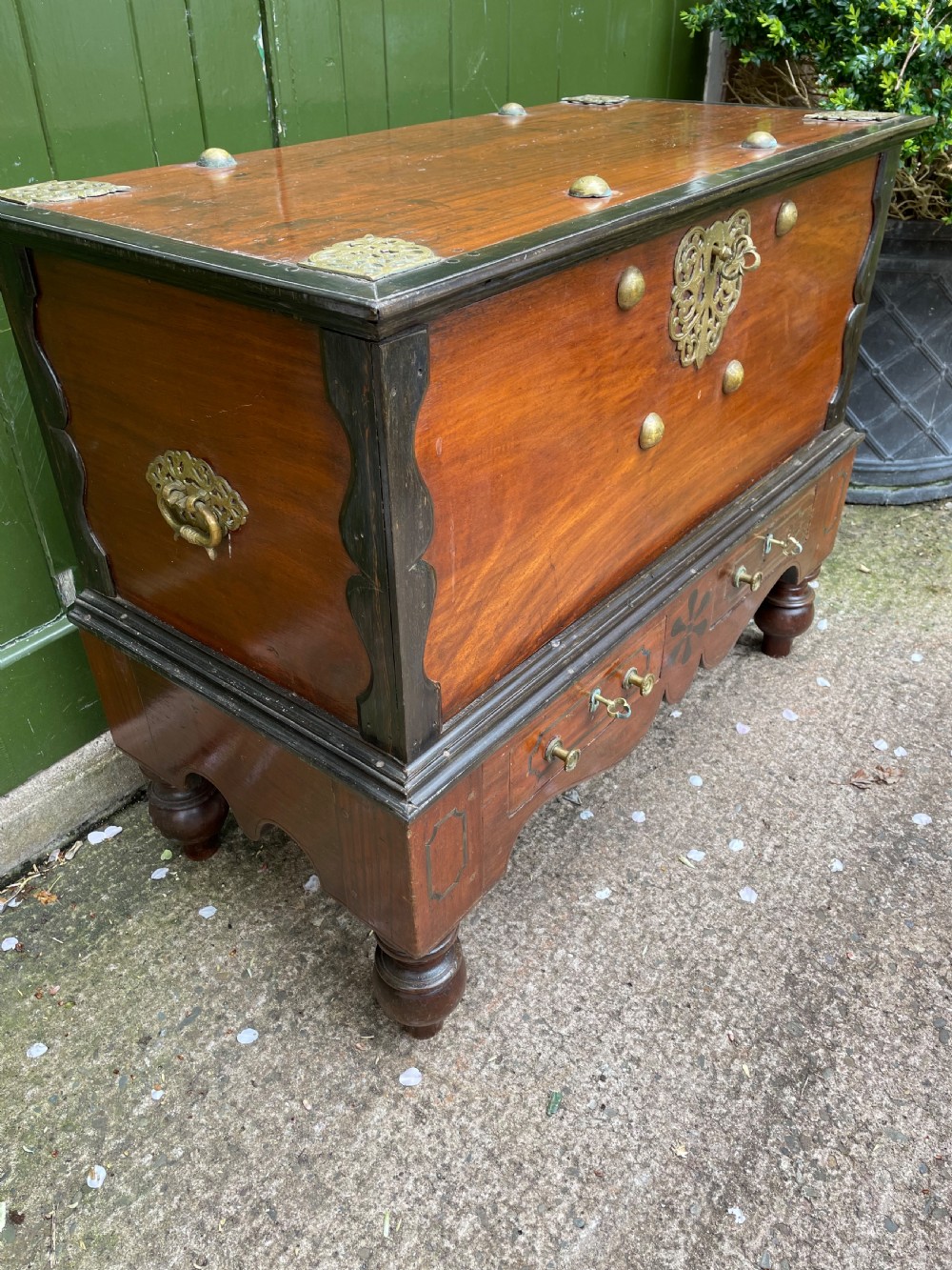 A 19th-century Dutch colonial teak and ebony chest with a pierced brass escutcheon, mounted on a two-drawer base with turned feet. View II