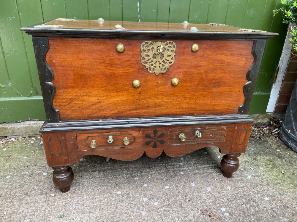 A 19th-century Dutch colonial teak and ebony chest with a pierced brass escutcheon, mounted on a two-drawer base with turned feet. View VI