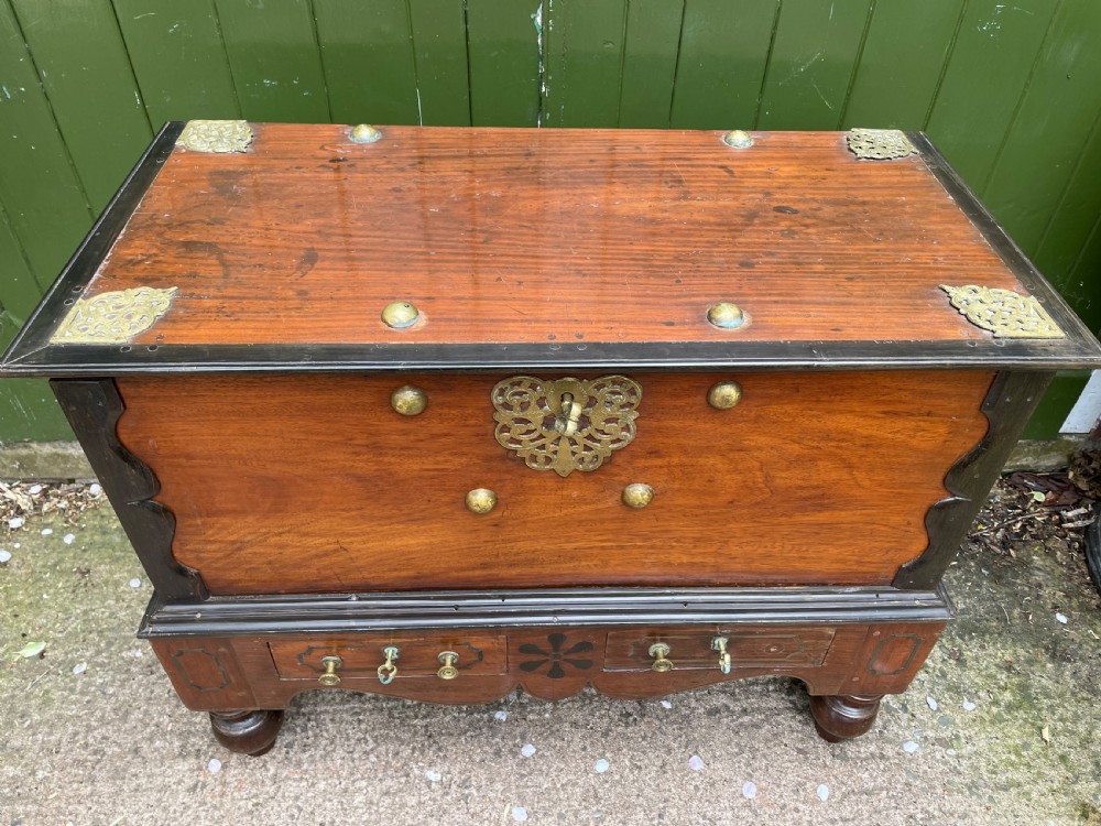 A 19th-century Dutch colonial teak and ebony chest with a pierced brass escutcheon, mounted on a two-drawer base with turned feet. View VII
