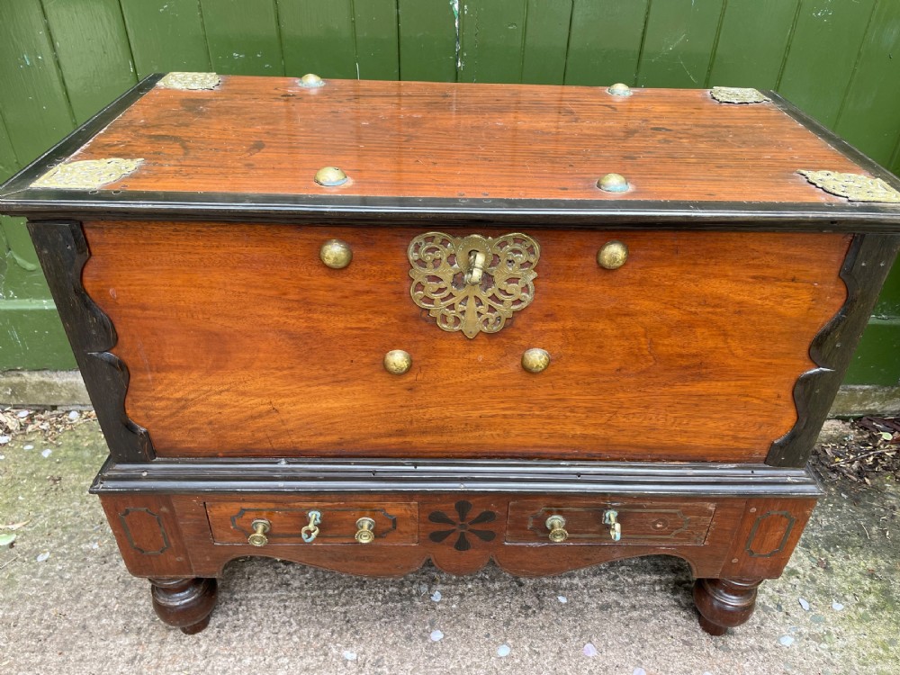 A 19th-century Dutch colonial teak and ebony chest with a pierced brass escutcheon, mounted on a two-drawer base with turned feet. View XI