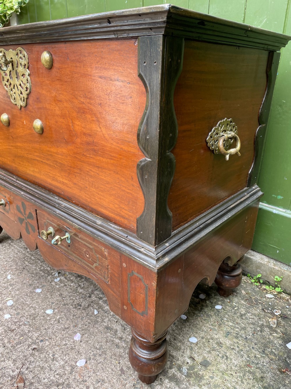 A 19th-century Dutch colonial teak and ebony chest with a pierced brass escutcheon, mounted on a two-drawer base with turned feet. View XII