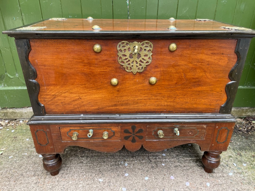 A 19th-century Dutch colonial teak and ebony chest with a pierced brass escutcheon, mounted on a two-drawer base with turned feet. View XV