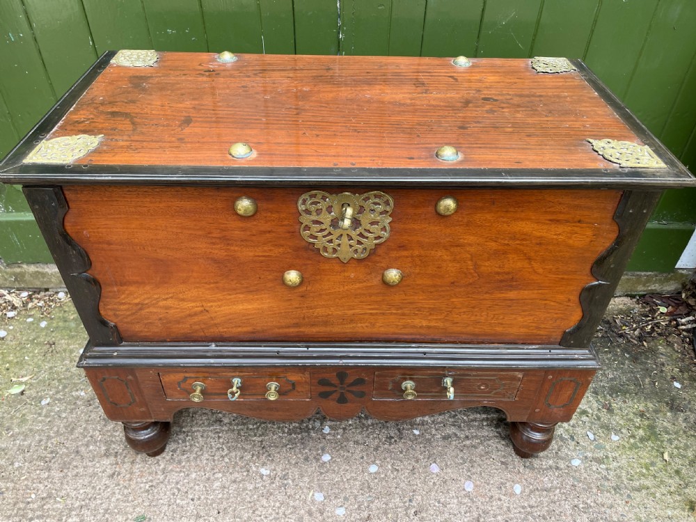 A 19th-century Dutch colonial teak and ebony chest with a pierced brass escutcheon, mounted on a two-drawer base with turned feet. View XVI