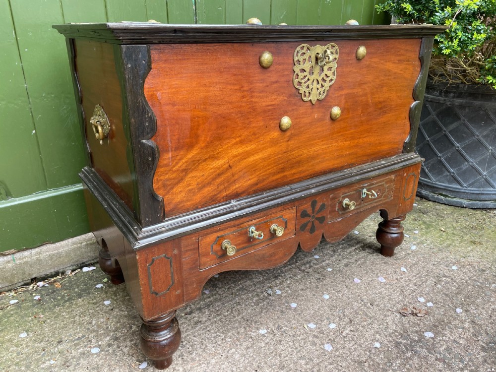 A 19th-century Dutch colonial teak and ebony chest with a pierced brass escutcheon, mounted on a two-drawer base with turned feet. View XVII