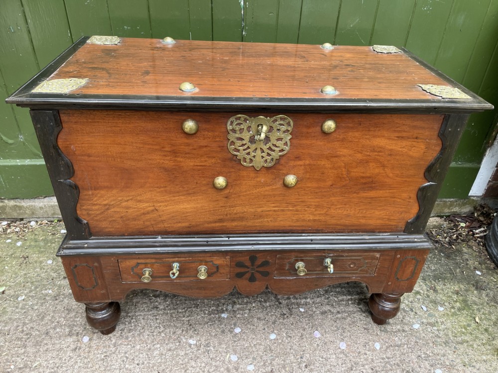 A 19th-century Dutch colonial teak and ebony chest with a pierced brass escutcheon, mounted on a two-drawer base with turned feet. View XVIII